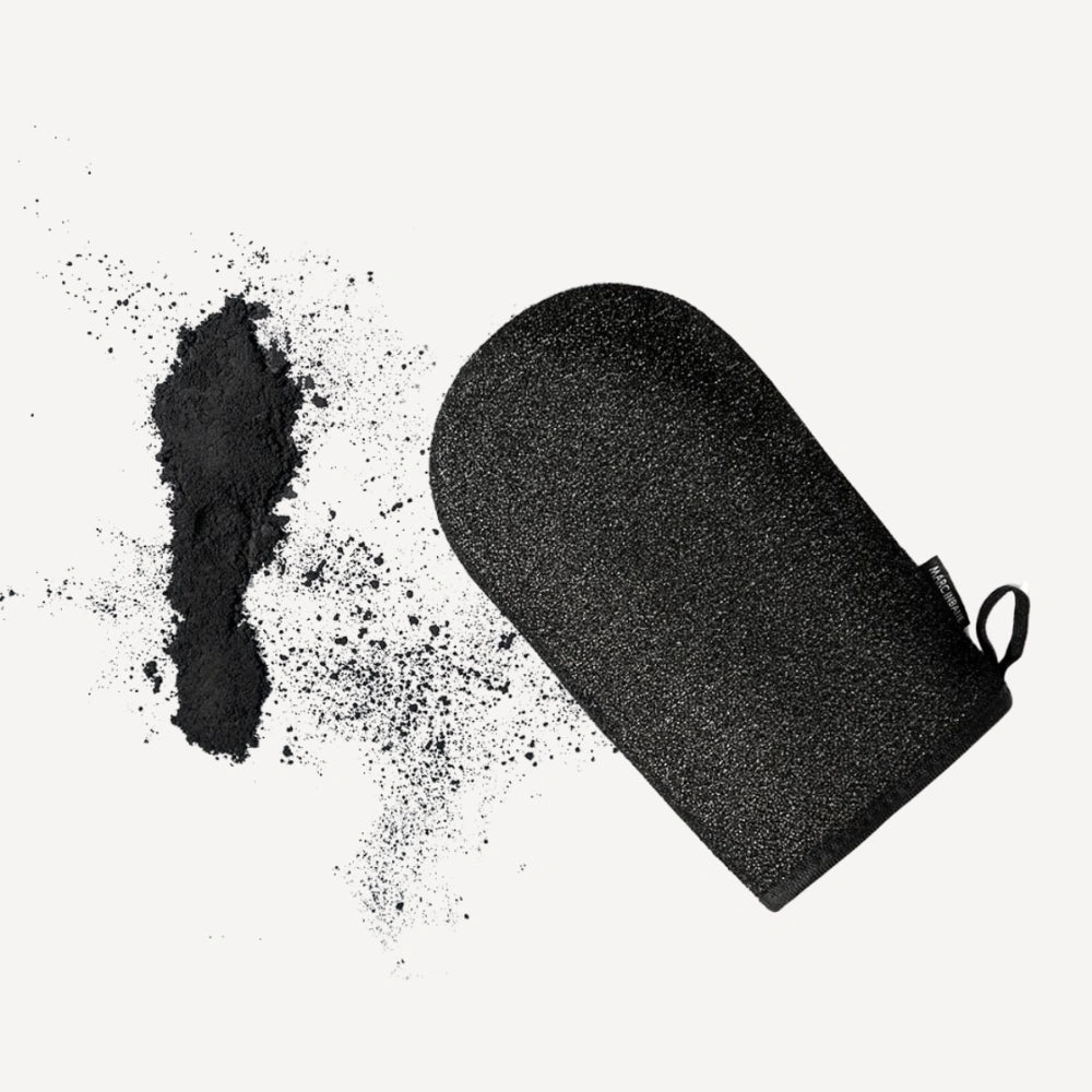 Marc Inbane Exfoliating Glove placerad på vit bakgrund med exfolierande kolpulver, visar handske för djupgående hudrengöring