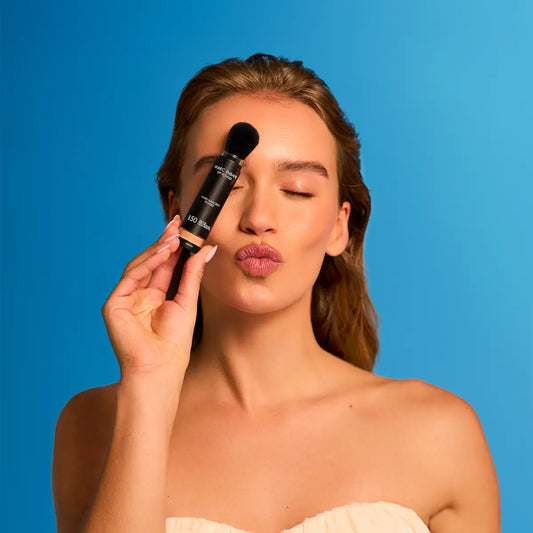 Leende kvinna håller upp Marc Inbane SPF Powder SPF50 mot ansiktet – tinted sunscreen powder för dagligt skydd och jämn hudton.