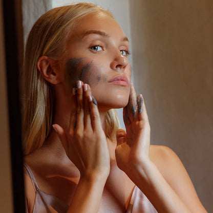 Kvinna applicerar Marc Inbane Black Exfoliator i ansiktet för att rengöra porer och återställa hudens lyster.